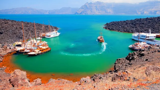 Traditional sailing boat cruising through the Santorini caldera with volcanic cliffs and blue Aegean Sea