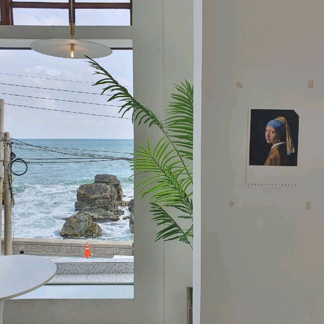 카페 우리집 내부에서 본 바다 — 창 프레임 사이로 보이는 바위와 파도
