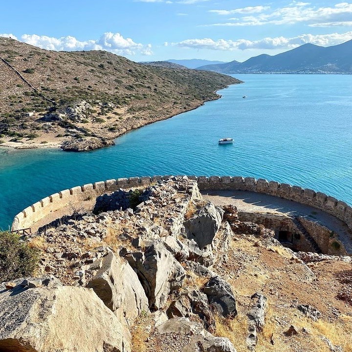 Spinalonga is an arid and barren rocky islet with an area of 8.5 hectares lying at the mouth of the natural port of Elounda in the Lasithi prefecture of Crete. Due to its strategic location, it was fortified and served a variety of roles and purposes over the centuries.
Spinalonga
“Spinalonga. She played with the word rolling it around her tongue like an olive stone. The island lay directly ahead and as the boat approached the great Venetian fortification which fronted the sea […]. This, she speculated, might be a place where history was still warm, not stone cold, where the inhabitants were really not mythical”....
... as Victoria Hislop wrote in her best-selling book “The Island”. 
Here, on an island where lepers from Crete and the rest of Greece had been kept in isolation until 1957, a story about love and pain, separation and fear was born.
Although it is small and known as the island of the outcasts, Spinalonga has a rather interesting story to tell. The island forms a natural defence “mechanism” for Elounda harbour, and in 1579 the Venetians built a mighty fortress here on the ruins of an ancient acropolis. The Venetians kept control of the island even after the rest of Crete fell to the Ottomans in 1669 and it remained under their control for almost another half a century until its capitulation in 1715. Today thousands of tourists visit Spinalonga by boat from Ayios Nikolaos, Elounda and Plaka each summer as it is the most popular archaeological site in Crete after Knossos.
A walk around Spinalonga –with some of the finest views of the clear blue waters that surround the island– will guide you through the pages of the novel. Strolling around the island takes about an hour, but the serenity of the place and the remnants of its recent history will certainly tempt you into spending much longer. A left turn by the old town hall takes you down to the beautiful seafront; take advantage of the opportunity to take some time for a swim.
#mynovgetaway 
#mynovgetaway