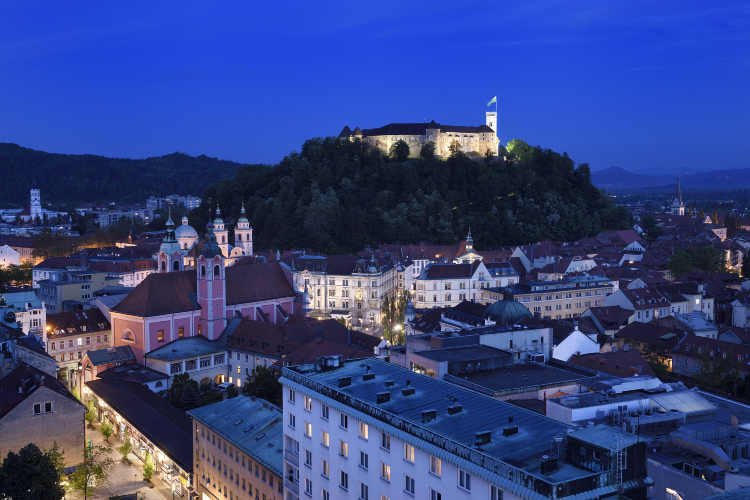 Ljubljana at dusk — the castle lit above the old town, the Ljubljanica river winding below