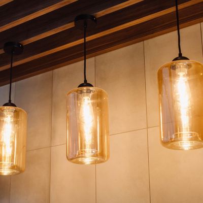 three hanging light fixtures , each with a glass shade and wooden frame , are mounted on a beige wall at Oval Hotel at Adelaide Oval, an EVT hotel