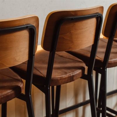 three wooden chairs with black metal frames are lined up against a white wall in a room at Oval Hotel at Adelaide Oval, an EVT hotel