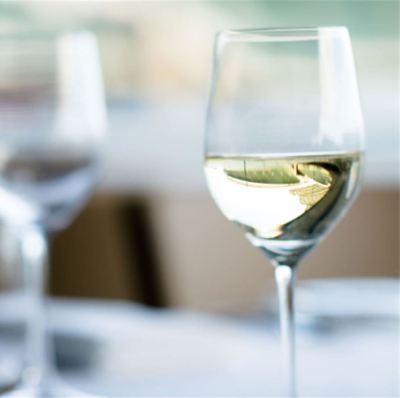 a glass of white wine is sitting on a dining table with other glasses in the background at Oval Hotel at Adelaide Oval, an EVT hotel