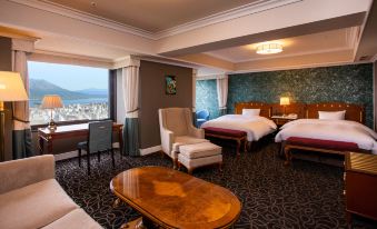a luxurious hotel room with a large bed , two chairs , and a balcony overlooking the city at SHIROYAMA HOTEL kagoshima
