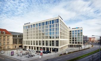 a modern building with a large glass facade is situated on a street corner near a parking lot at HYPERION Hotel Leipzig