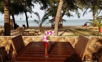 a wooden dining table with a vase of flowers in the center , set near a beach and overlooking the ocean at Ao Thai Resort