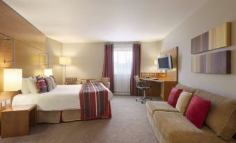 a hotel room with a bed , couch , and desk , all arranged in a well - organized arrangement at Ramada Plaza by Wyndham Wrexham