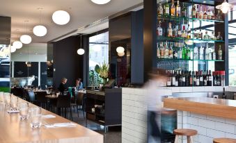 a modern restaurant with a long dining table and several chairs , as well as a bar area with a variety of bottles and glasses at The Cullen Melbourne - Art Series