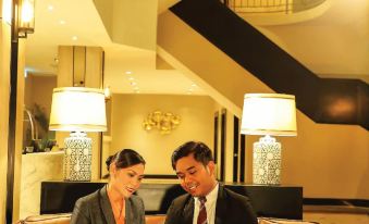 a man and a woman are sitting on a couch in a hotel lobby , with the woman holding an ipad at RHR Hotel Kajang