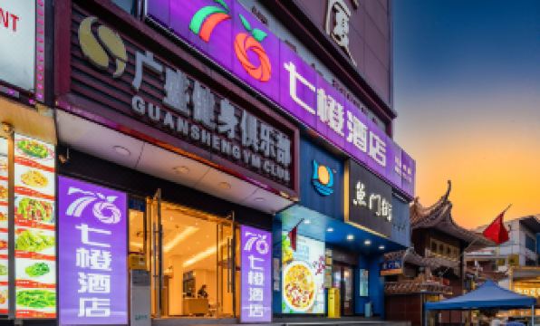 At night, a building with illuminated signs stands out among other buildings in the background, creating a vibrant and lively atmosphere at Seven Orange Hotel (Guangzhou Railway Station)