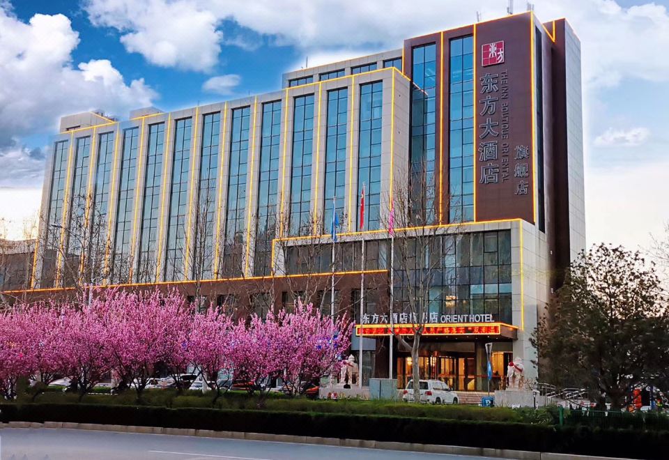 a modern building with a pink tree in front , under a blue sky with clouds at Orient Hotel