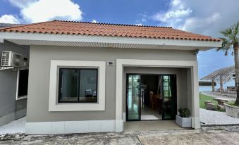 a small , two - story house with a red tile roof and white walls , situated on a dirt road at Baan Tah on the Sea