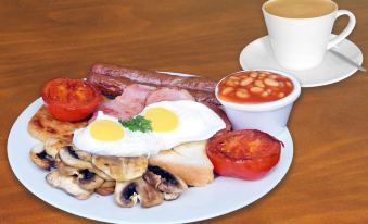 a delicious breakfast on a dining table , consisting of eggs , bacon , sausage , mushrooms , toast , and tomato juice at Mandarin Motel