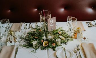 a table is set with a centerpiece made of greenery and candles , along with silverware and wine glasses at Copper Beech Inn