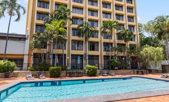 a large hotel with a swimming pool in front of it , surrounded by palm trees at Frontier Hotel Darwin