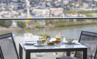 a table with breakfast items and a cup of coffee is set on a balcony overlooking a cityscape at The Milton Brisbane