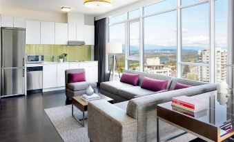 a modern living room with a large window and couch , purple cushions , and white cabinets at Element Vancouver Metrotown