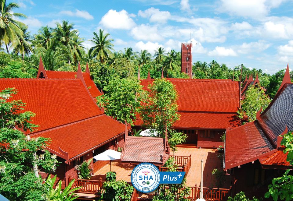 a tropical resort with red - roofed buildings , surrounded by lush greenery and palm trees under a clear blue sky at Baan Amphawa Resort & Spa