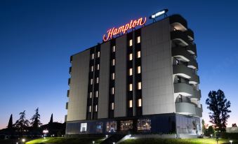 "a large , modern hotel building with a red sign that reads "" hampton inn "" lit up at night" at Hampton by Hilton Rome North Fiano Romano