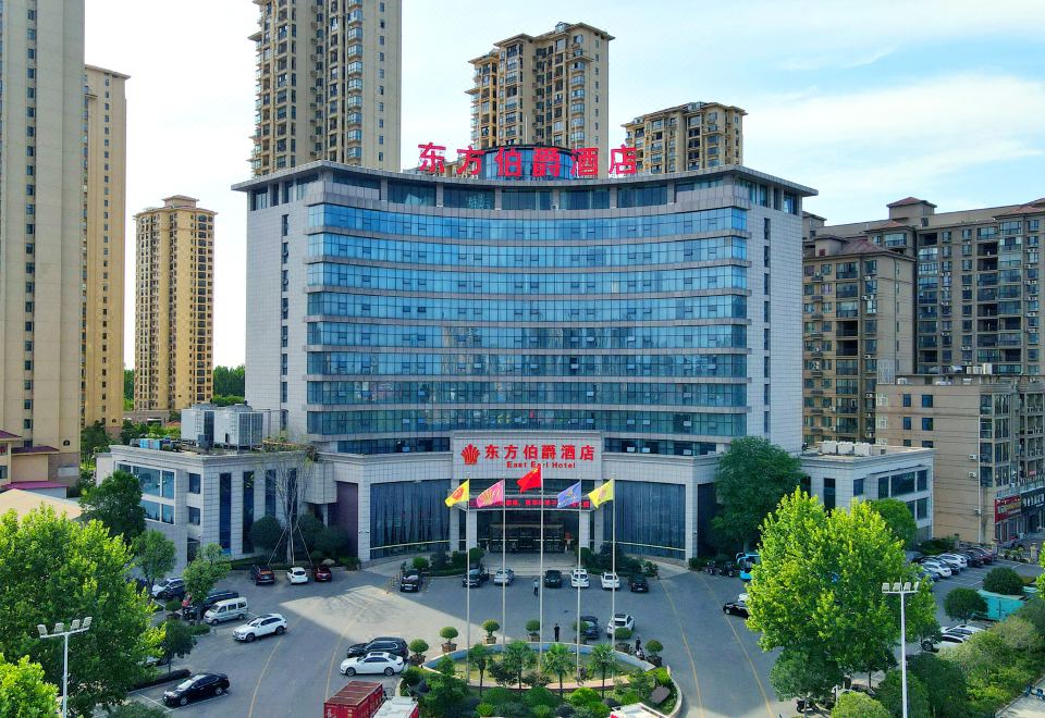 a large hotel building surrounded by trees , with a car parked in front of it at Gushi Oriental Earl Hotel (Yucheng Avenue Genqin Culture Park)