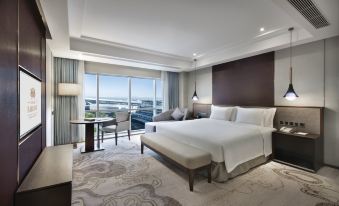 The bedroom features large windows and a balcony that overlook the city, with a bed positioned in front at Grand Barony Qingdao Airport Hotel