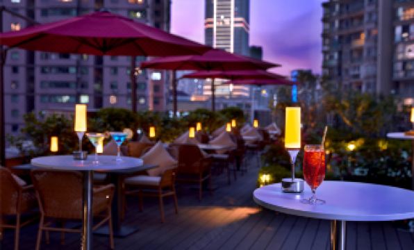 At night in the city center, there are outdoor tables and chairs with umbrellas on a deck at THE ONE Shanghai Downtown Vignette Collection by IHG