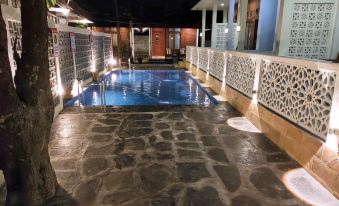 a large swimming pool is surrounded by a stone patio with white railings and lights at The Royal Joglo