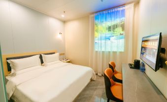 A bedroom with a double bed, desk, and chair is located by a large window at Jingu Business Hotel (Chigang Subway Station, Guangzhou Weizhou Convention and Exhibition Center)