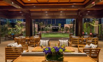 a spacious room with wooden furniture , including chairs and tables , surrounded by potted plants and a view of a garden at Grand Hyatt Manila