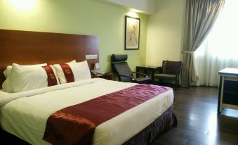 a large bed with a maroon blanket and white sheets is in a room with wooden floors at Palm Seremban Hotel
