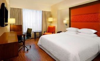 a large bed with white linens is in a hotel room with wooden floors and chairs at Four Points by Sheraton Ahmedabad