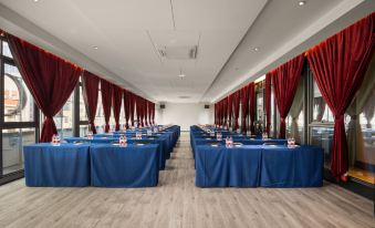 a large conference room with multiple blue tables and red curtains , set up for a meeting at Mehood  Lestie Hotel