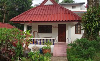 a small white house with a red roof , situated in a lush green garden near a body of water at Top Resort