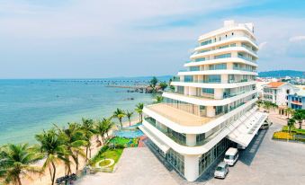 a large white building with a parking lot in front of it , surrounded by palm trees and a body of water at Seashells Phu Quoc Hotel & Spa