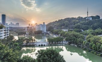 a serene landscape of a city park with a lake , buildings , and trees during sunset at Atour Hotel