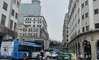 A busy city street with pedestrians crossing and buses on both sides, surrounded by tall buildings at Yue City Youth Apartment