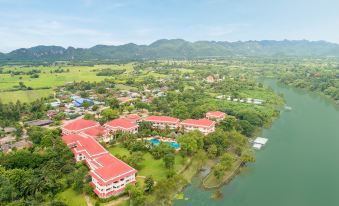 aerial view of a resort surrounded by mountains and a river , with multiple buildings and trees in the background at Dheva Mantra Resort