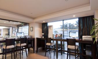 a modern office space with large windows , wooden tables and chairs , and a variety of items on the desk at Copthorne Hotel Wellington, Oriental Bay