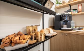 a kitchen counter with various types of bread , pastries , and coffee cups , along with a microwave oven at Hotel Carlton