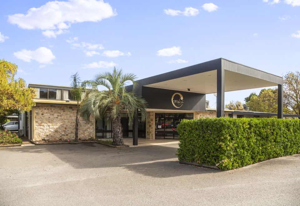 a modern , black - and - white building with a large tree in front of it , surrounded by grass and palm trees at The Wine Vine Hotel