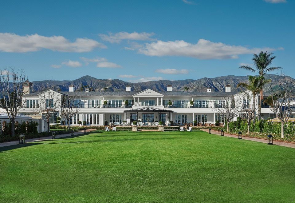 a large white building with a green lawn in front of it and mountains in the background at Rosewood Miramar Beach