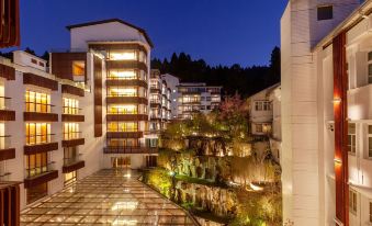 a modern building with multiple floors , surrounded by trees and lit up at night , under a blue sky at Alishan House