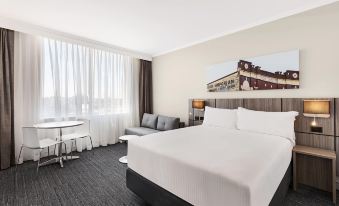 a large , neatly made bed is in the middle of a hotel room with a couch and a window at Mercure Sydney Bankstown