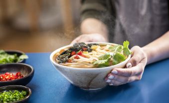 A person is holding up food in front of them while there is another bowl with soup on the table next to them at Holiday Inn Express Chengdu West Gate