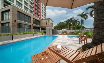 a large outdoor swimming pool surrounded by a patio area , with several lounge chairs and umbrellas placed around the pool at Travelodge Ipoh