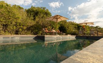 a man and a woman sitting on lounge chairs by a pool , enjoying the view of the lake at Pumba Private Game Reserve