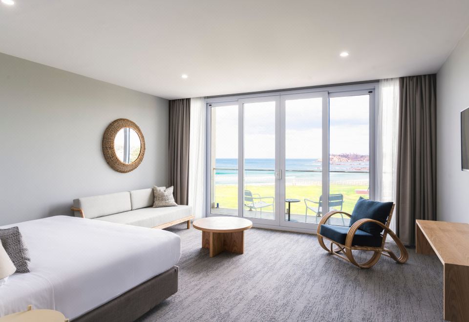 a modern bedroom with a large window overlooking a beautiful view of the ocean , accompanied by a couch and a chair at Abode Malua Bay