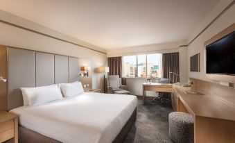 a large bed with white linens is in a room with a desk and chair at Stamford Plaza Adelaide