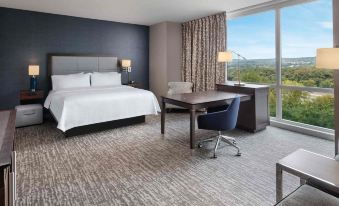 a modern hotel room with a large window offering a view of the city , white bed , desk , and chairs at Hampton Inn & Suites Teaneck Glenpointe