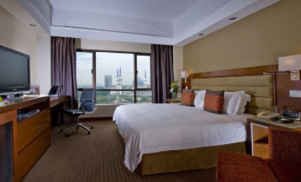 a large bed with white sheets and orange pillows is in a room with a chair , table , and windows at Concorde Hotel Shah Alam